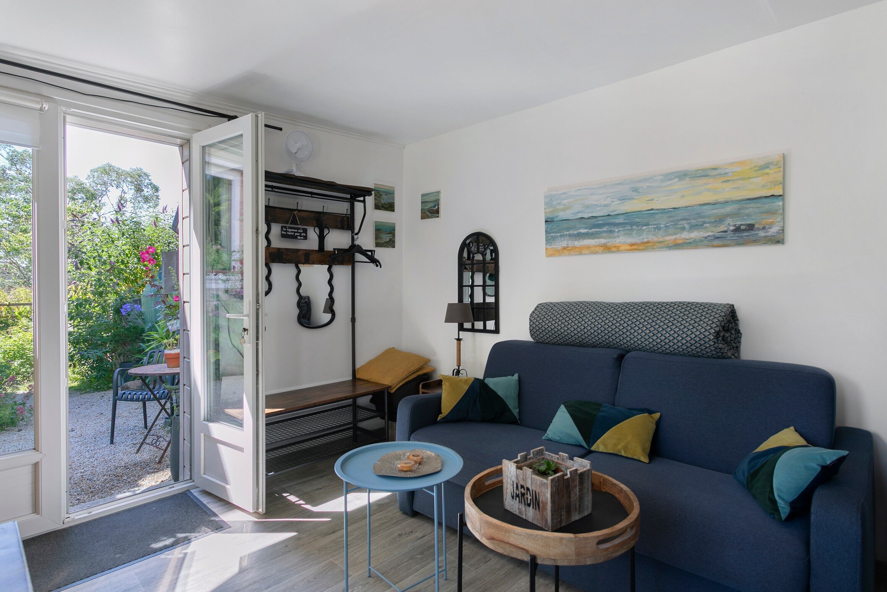 A living room with a blue sofa, a small round table, and a door leading to a garden.