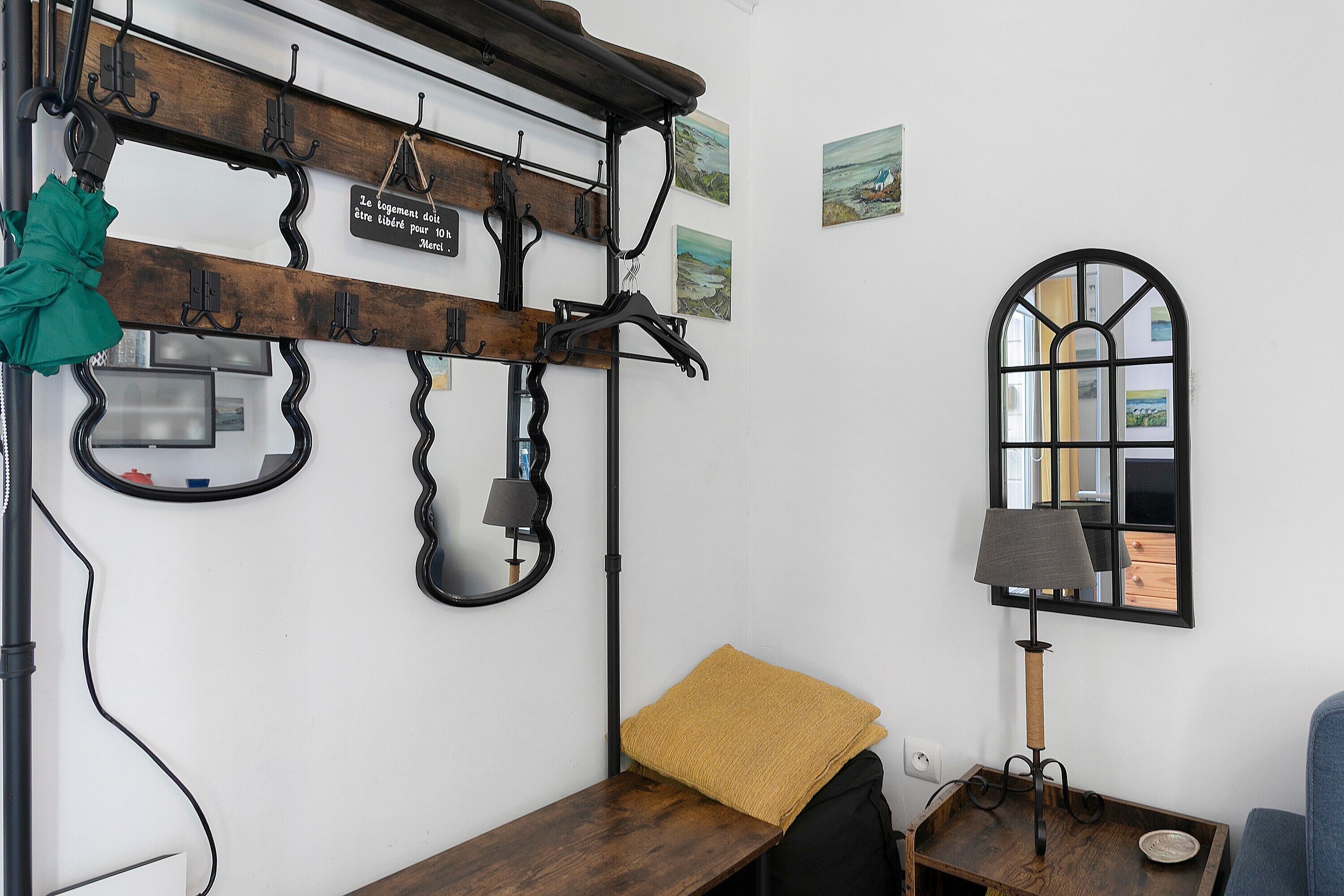 Una habitación con un banco de madera, un espejo, una lámpara y un perchero con ganchos.