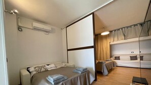 A modern hotel room with a bed, a sofa, a small table, and a ceiling-mounted air conditioning unit. - Casa Lily 2: A Cozy Apartment with a View. (DIANO CASTELLO)