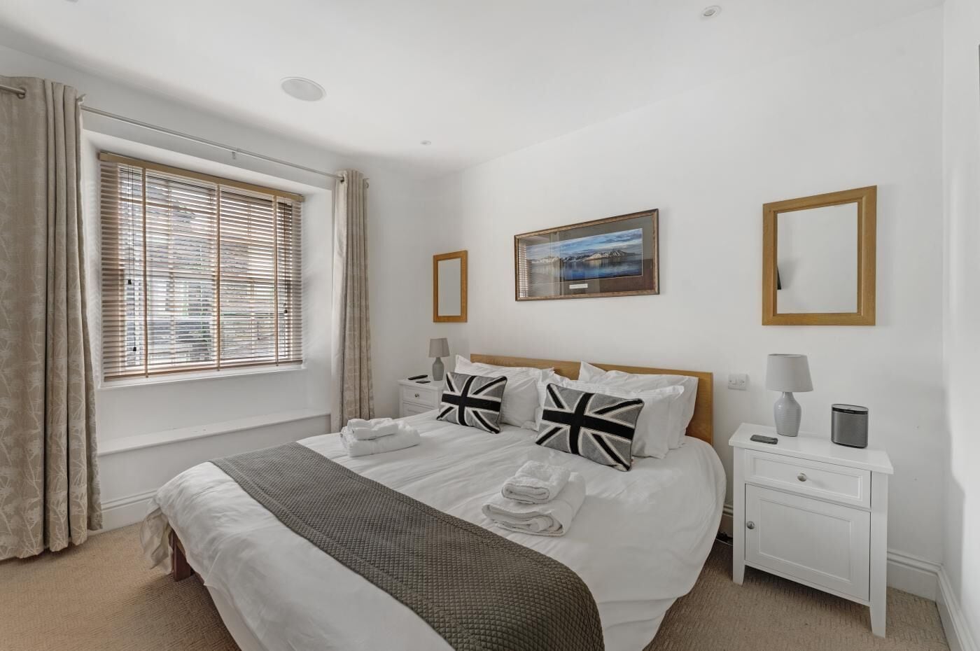 A neatly arranged bedroom with a bed, bedside tables, a window with blinds, and a framed picture on the wall.