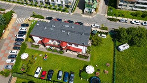 Ein Luftbild eines Wohngebiets mit einem Haus mit rotem Dach, einem Parkplatz mit mehreren Autos und einer kleinen Grünfläche.