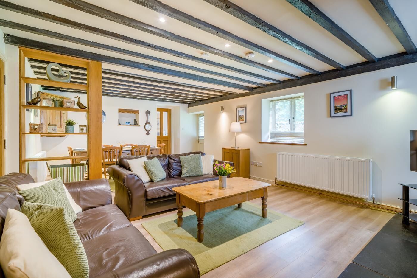 A cozy living room with a brown leather sofa, a wooden coffee table, and a dining area with wooden chairs and a table.
