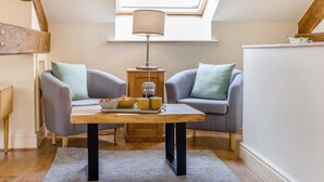 Ein gemütliches Zimmer mit Oberlichter, zwei grauen Sessel, einem Holztisch mit einer Serviertafel und einer Stehlampe.
