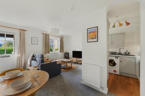 Ein modernes Wohnzimmer mit Sofa, Fernseher und Essbereich mit Tisch für zwei Personen.