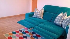 En turkosfärgad soffa med kuddar i rutmönster, en färgglad, geometrisk matta och ett trägolv.