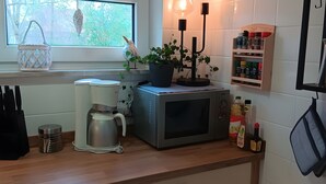 Ett kök med en kaffebryggare, en mikrovågsugn, en vattenkokare, en krukväxt och ett kryddställ.