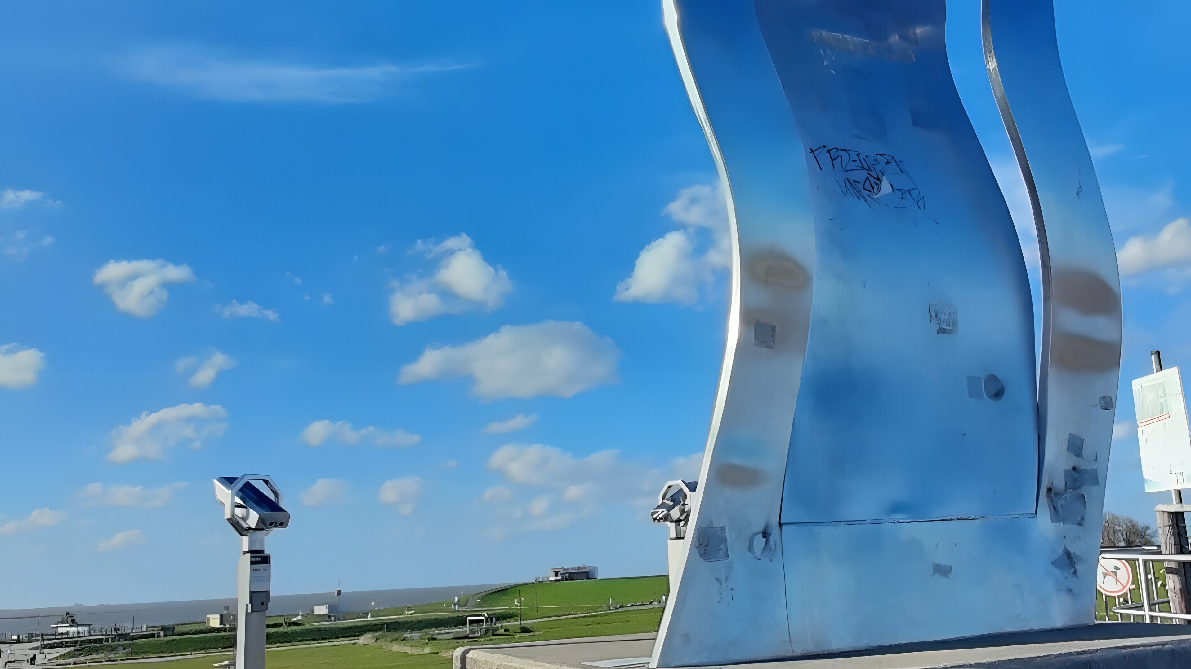A modern architectural structure with a curved design, a solar panel, and a clear blue sky with clouds.