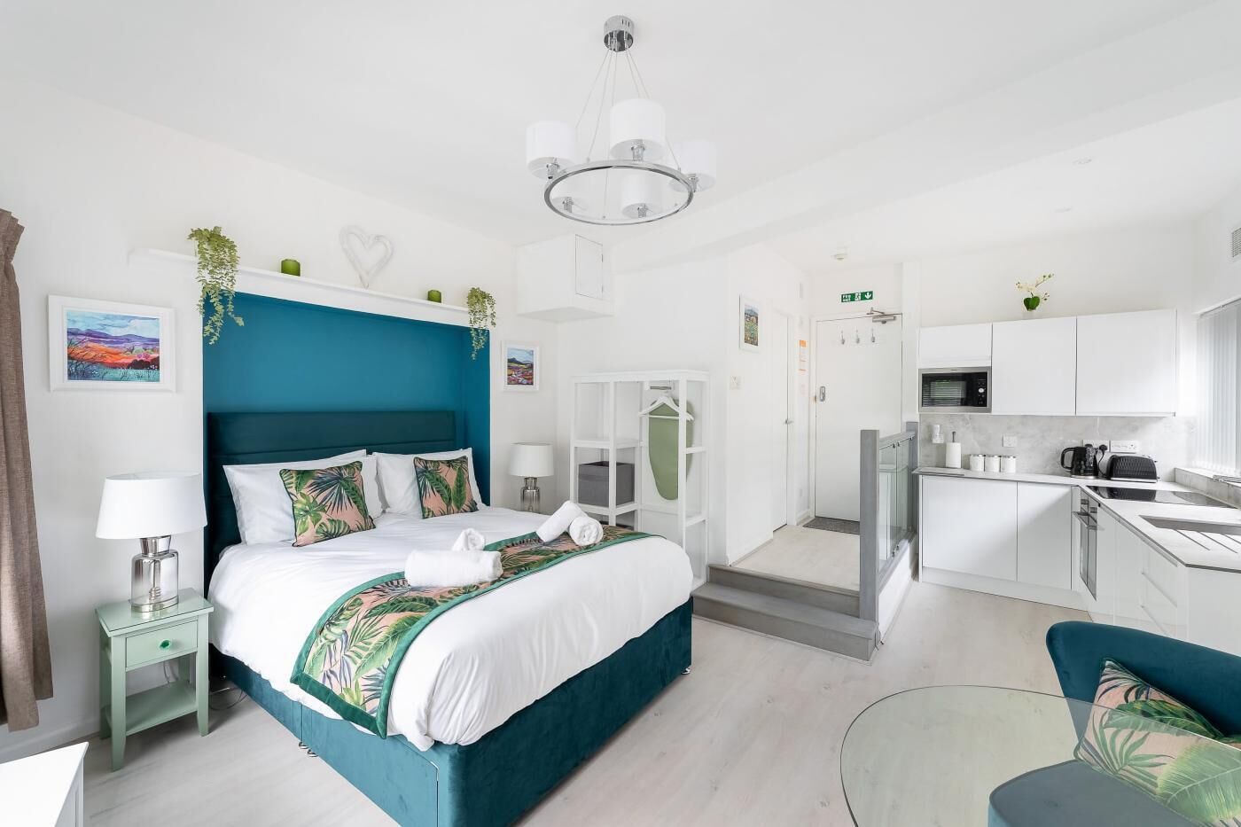 A modern hotel room with a large bed, a separate kitchen area, and a view of the city.