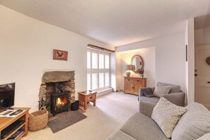 A cozy living room with a fireplace, a sofa, a television, and a window with shutters. - 1 Bed in Ambleside (oc-lr058) (Ambleside)