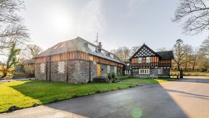 Uma casa de pedra tradicional com telhado inclinado e um edifício menor adjacente com estrutura de madeira aparente.
