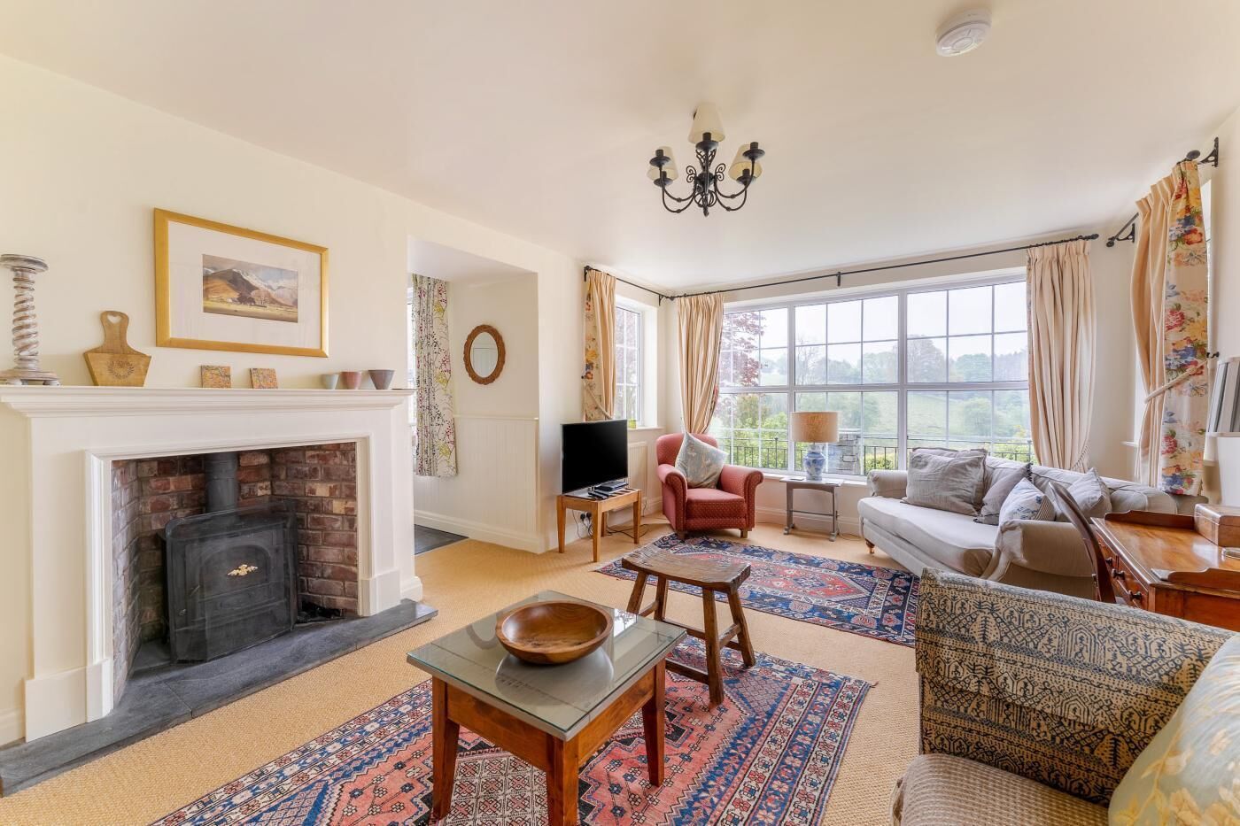 A living room with a fireplace, a sofa, a TV, and a large window with curtains.