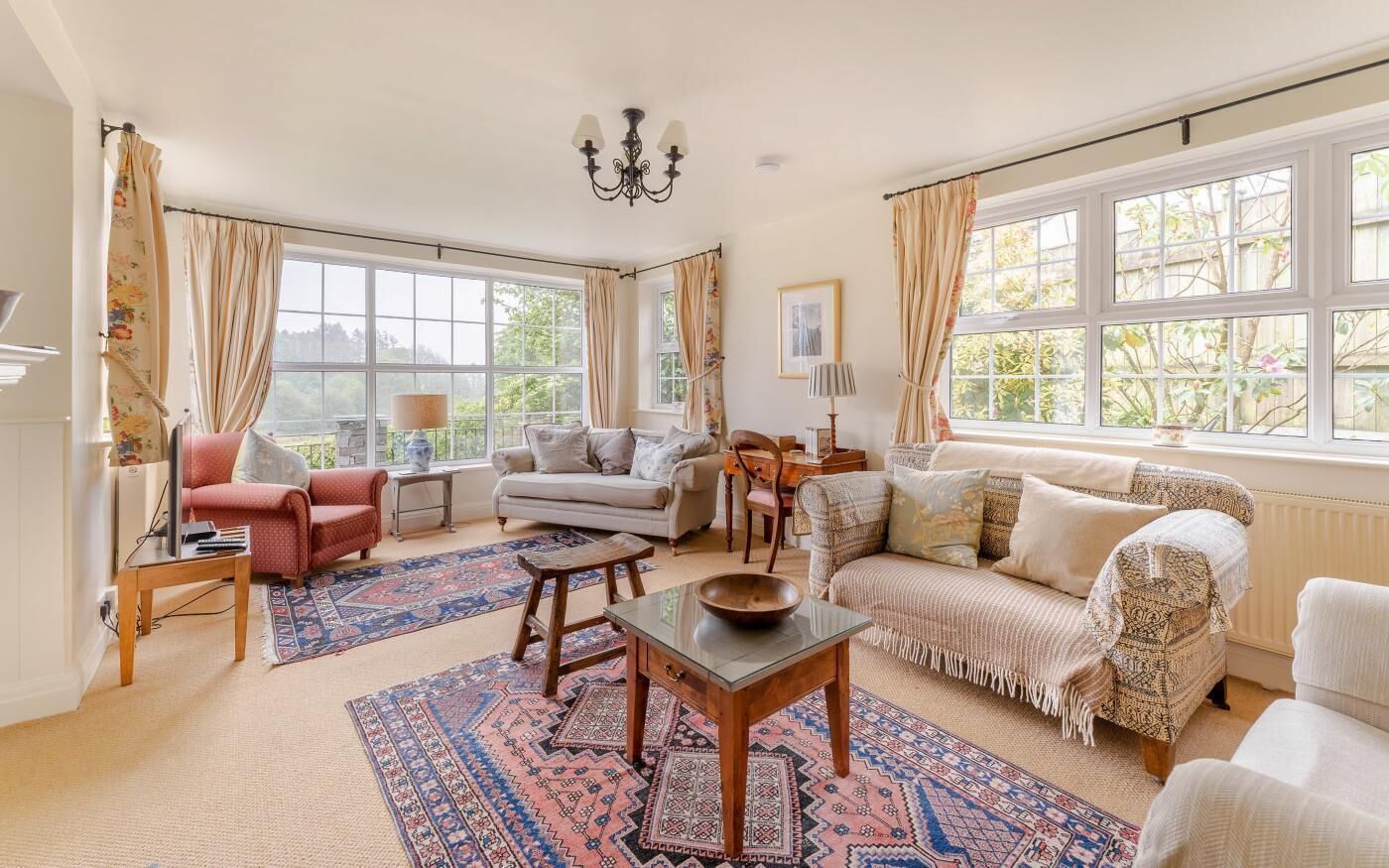 A well-lit living room with a sofa, armchairs, a coffee table, and a patterned rug.