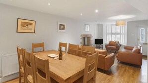 A dining area with a wooden table and chairs, a fireplace, a television, and a seating area with leather sofas. - 4 Bed in Ambleside (oc-lr034) (Ambleside)