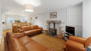 A living room with a fireplace, leather sofas, a television, and a dining area with wooden furniture. - 4 Bed in Ambleside (oc-lr034) (Ambleside)
