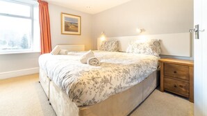 A bedroom with a large bed, a nightstand, a window with curtains, and a wall-mounted picture. - 4 Bed in Ambleside (oc-lr034) (Ambleside)