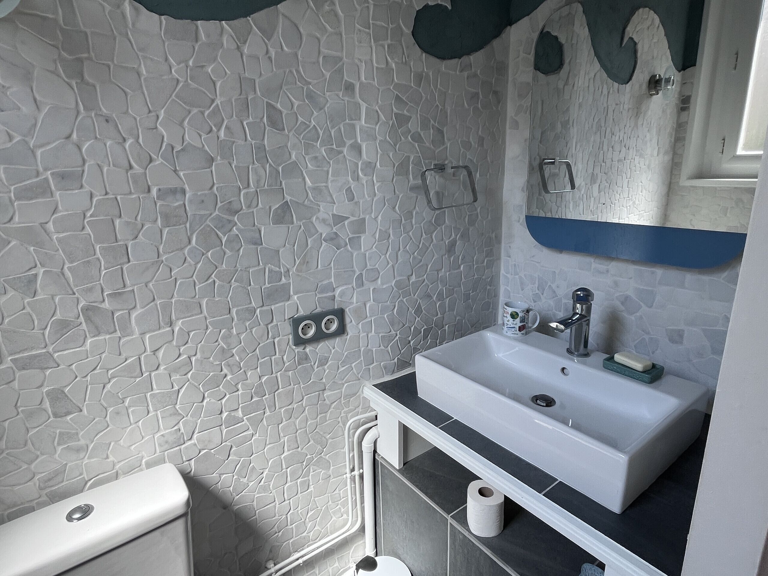 A bathroom with a stone-patterned wall, a white sink, a mirror, and a toilet.