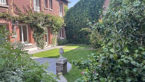 Un edificio de ladrillo con un jardín bien cuidado, una barandilla de piedra y un seto.