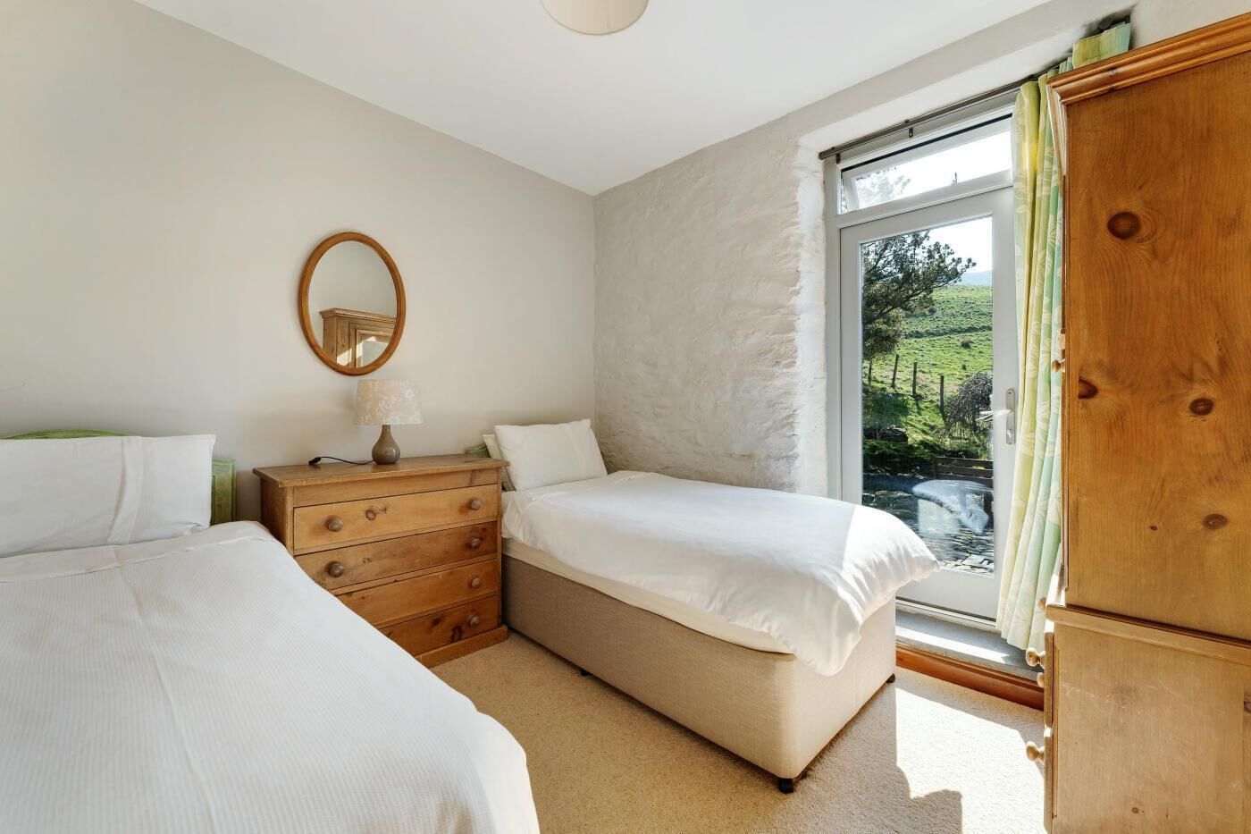 A bedroom with two beds, a dresser, a mirror, and a window with a view of greenery.
