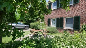 A brick house with a car parked in the driveway, a wooden bench, and a garden with various plants.