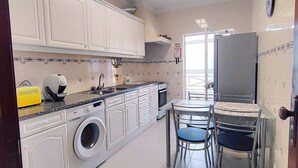 A compact kitchen with a washing machine, a sink, and a dining area with chairs. - Apartment 'Casa Várzea' with Wi-Fi (Lagos)