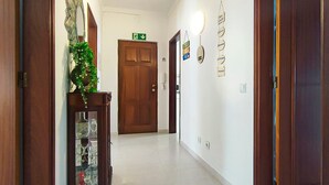 A hallway with a wooden door, a green emergency exit sign, and a wall-mounted light fixture. - Apartment 'Casa Várzea' with Wi-Fi (Lagos)