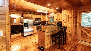 Interior de una cabaña de madera con cocina equipada, que incluye un refrigerador, microondas, estufa y taburetes de bar.