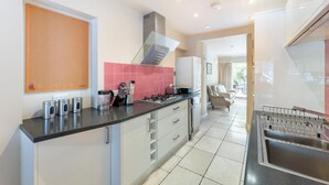 Et moderne køkken med sort bordplade, rustfrie hvidevarer og en lyserød backsplash.