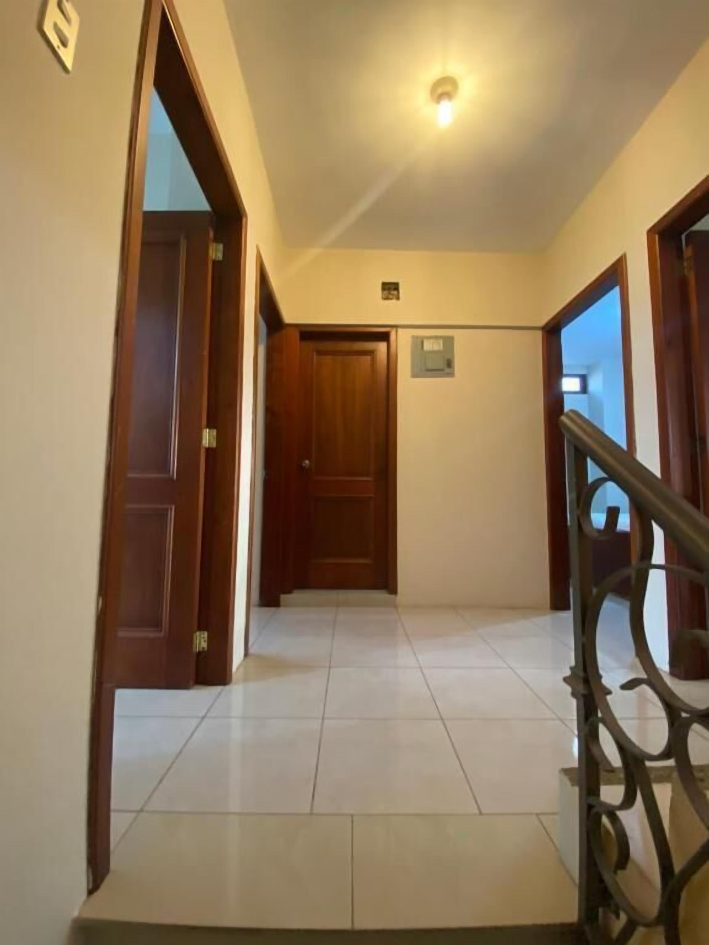 A hallway with a wooden door, a metal railing, and a tiled floor.