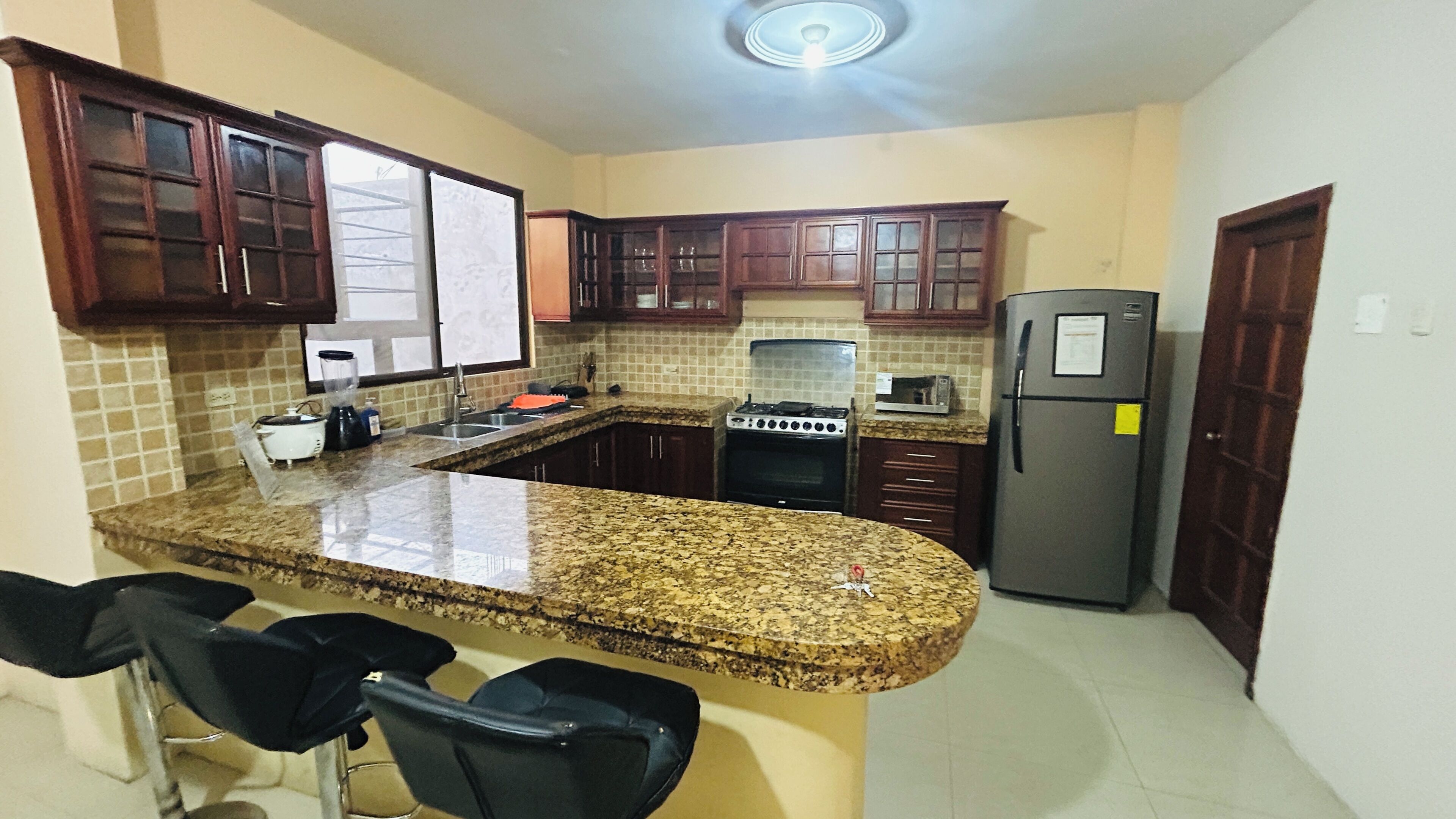 A kitchen with granite countertops, a refrigerator, a stove, and wooden cabinets.