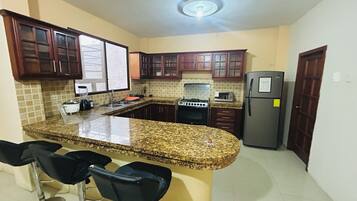 A kitchen with granite countertops, a refrigerator, a stove, and wooden cabinets.