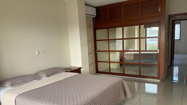 A bedroom with a bed, a nightstand, a wardrobe, and a sliding door leading to a balcony. - NCG Suite 2 (Guayaquil)