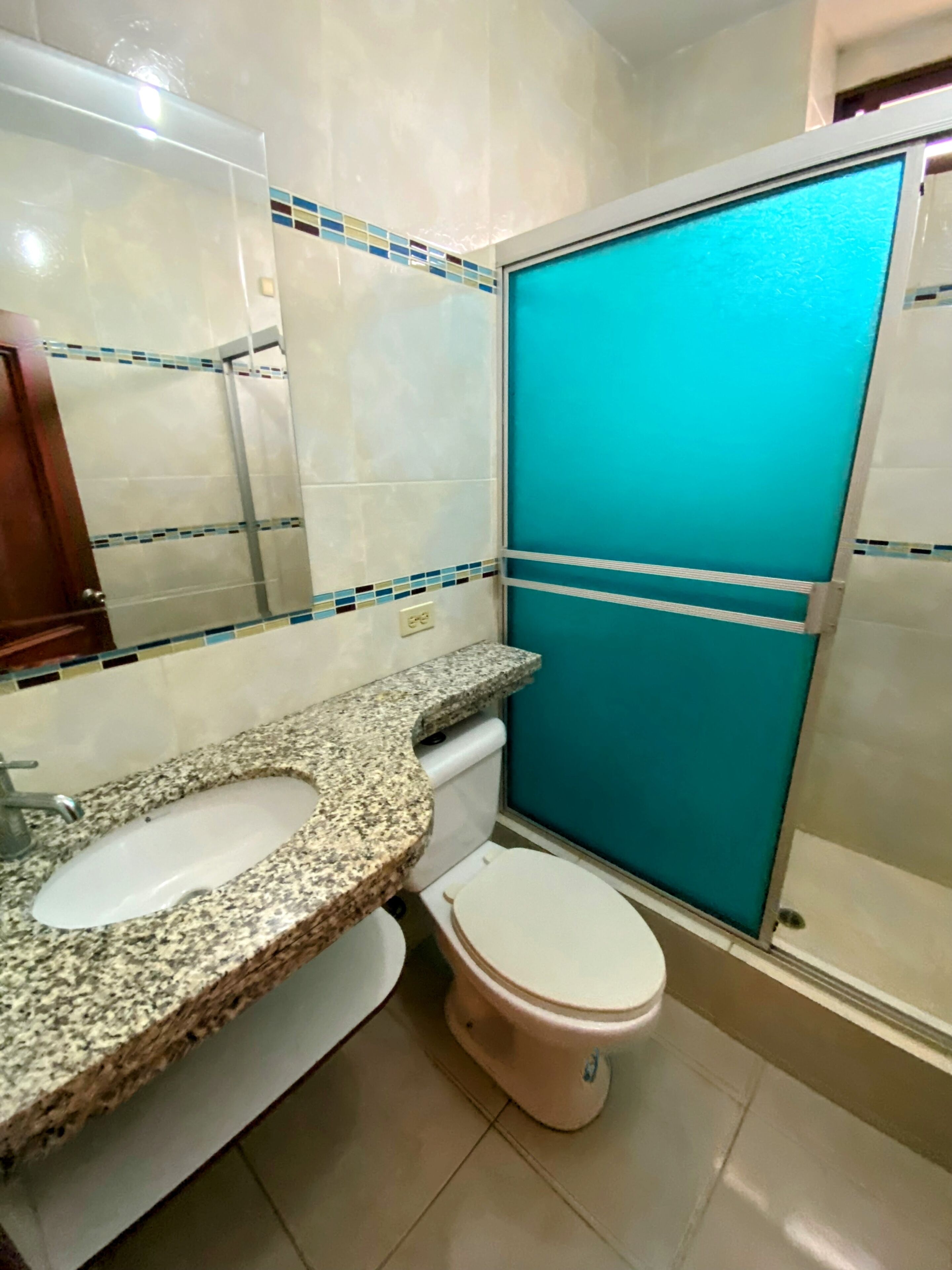 A bathroom with a granite countertop sink, a toilet, and a shower enclosure.