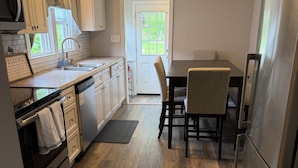 Une cuisine avec un plancher en bois, des armoires blanches, un réfrigérateur, un lave-vaisselle et un coin repas avec des chaises et une table.