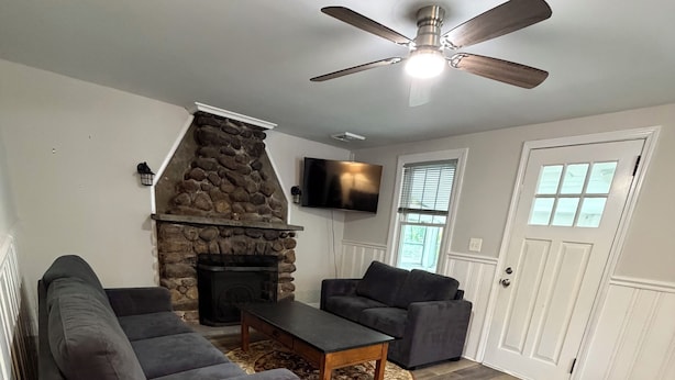 Un salon doté d’une cheminée en pierre, d’un ventilateur de plafond et d’un téléviseur fixé au mur.