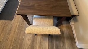 Une table à manger avec des bancs, un coin cuisine avec des meubles blancs et une porte équipée d’un extincteur.