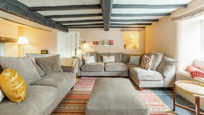 Ein Wohnzimmer mit einer Sofagarnitur, einem gemusterten Teppich und einer Holzbalkenkonstruktion an der Decke.