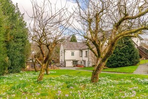 A white building with a traditional design, surrounded by a well-maintained garden with various trees and flowering plants. - 5 Bed in Hawkshead (oc-lr134) (Hawkshead)