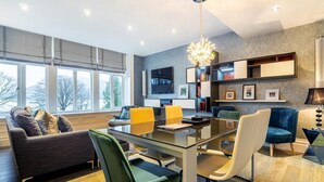 Ein modernes Wohnzimmer mit einem Glastisch, bequemen Sitzmöglichkeiten, einem Fernseher und einem Bücherregal.