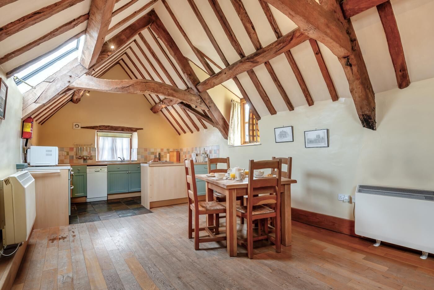 Une cuisine avec des poutres en bois, une table à manger avec des chaises, et une vue sur la pièce adjacente.