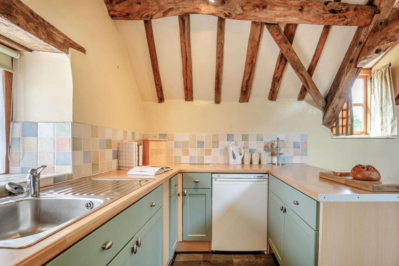 A kitchen with a wooden ceiling, a tiled backsplash, a sink, a dishwasher, and a window.