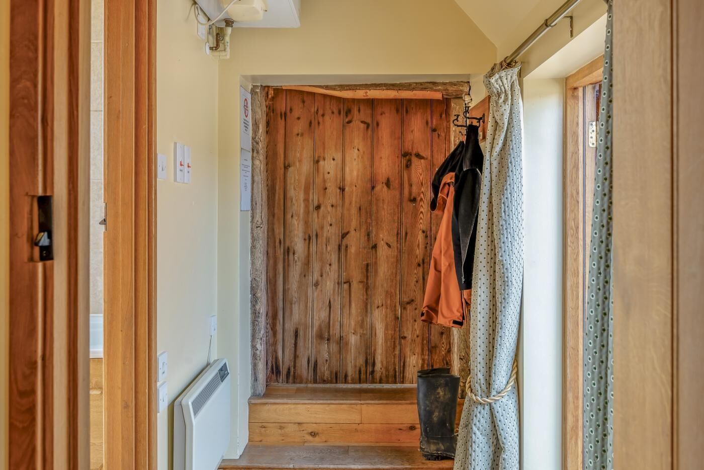 Een hal met houten wanden, een kapstok met kleding, een radiator en een deur.