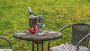 Ein runder Tisch im Freien mit einer Champagnerflasche, zwei Gläsern und einer Schale Erdbeeren.