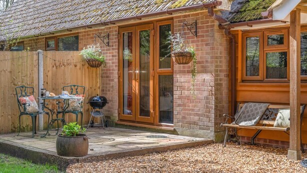 Une maison en briques avec un toit en tuiles, une clôture en bois, une terrasse avec une table et des chaises, et des jardinières suspendues.