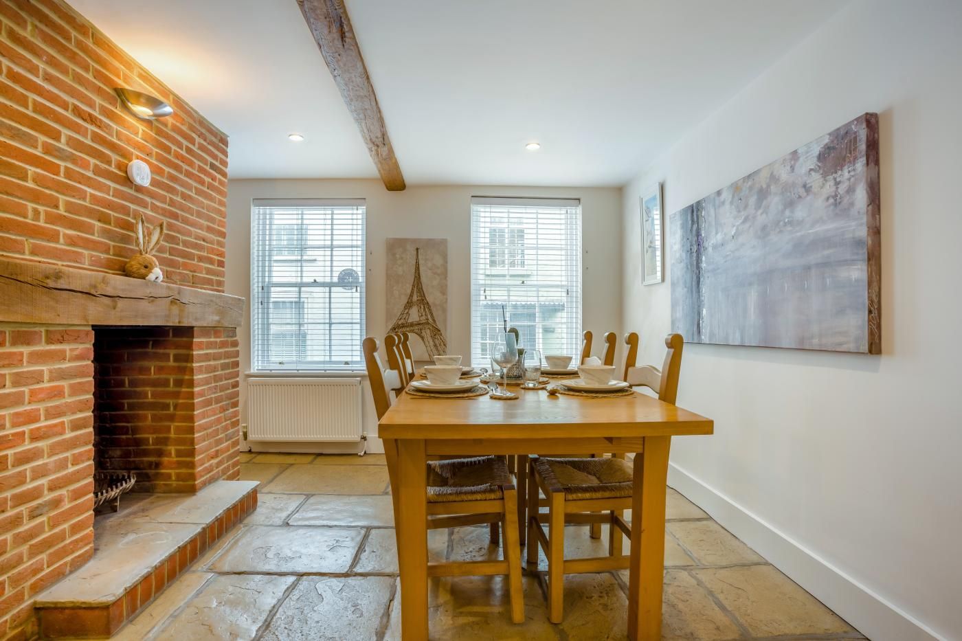 A dining area with a brick fireplace, a table set for four, and a large abstract painting on the wall.