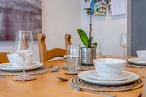 A dining table set with plates, bowls, cutlery, and glasses, with a plant centerpiece and a wall with papers in the background. - 4 Bed in Lymington (oc-c41423) (Lymington)