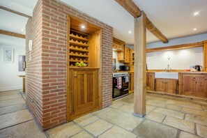 A kitchen with a brick wall, wooden cabinets, and a stone floor. - 4 Bed in Lymington (oc-c41423) (Lymington)