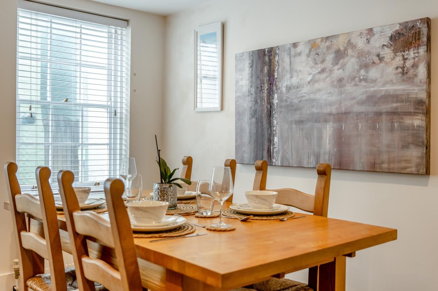 A dining area with a wooden table set for four, surrounded by wooden chairs.