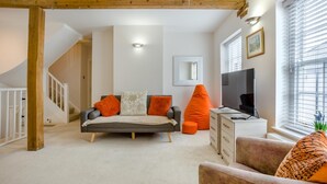 Un soggiorno moderno con un divano, pouf arancioni, una televisione e una scala.