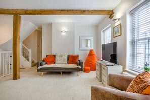 Ein modernes Wohnzimmer mit einer Couch, orangefarbenen Poufs, einem Fernseher und einer Treppe.