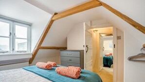 Una camera da letto con soffitto spiovente, un letto con copriletto color petrolio, due asciugamani a righe, un comò e una porta che dà su un'altra stanza.